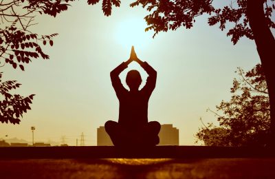 Silhouette of a person practicing yoga outdoors during sunrise, creating a calming atmosphere.
