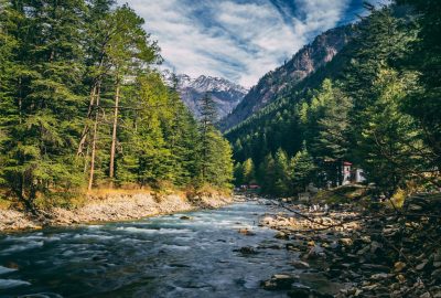 Beautiful landscape of river flowing through coniferous forest in Kasol, India with mountains in the background.
